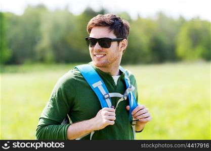 travel, hiking, backpacking, tourism and people concept - happy young man in sunglasses with backpack walking outdoors