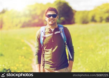 travel, hiking, backpacking, tourism and people concept - happy young man in sunglasses with backpack walking outdoors. happy young man with backpack hiking outdoors