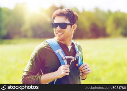 travel, hiking, backpacking, tourism and people concept - happy young man in sunglasses with backpack walking outdoors. happy young man with backpack hiking outdoors