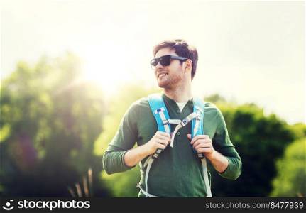 travel, hiking, backpacking, tourism and people concept - happy young man in sunglasses with backpack walking outdoors. happy young man with backpack hiking outdoors. happy young man with backpack hiking outdoors