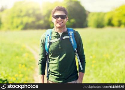 travel, hiking, backpacking, tourism and people concept - happy young man in sunglasses with backpack walking outdoors. happy young man with backpack hiking outdoors. happy young man with backpack hiking outdoors