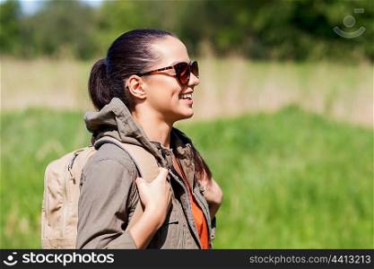 travel, hiking, backpacking, tourism and people concept - happy young woman in sunglasses with backpack walking outdoors