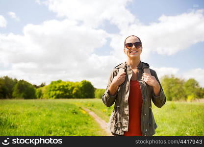 travel, hiking, backpacking, tourism and people concept - happy young woman in sunglasses with backpack walking along country road outdoors