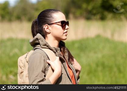 travel, hiking, backpacking, tourism and people concept - happy young woman in sunglasses with backpack walking along country road outdoors