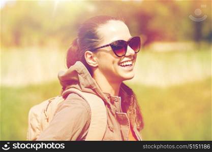 travel, hiking, backpacking, tourism and people concept - happy young woman in sunglasses with backpack walking along country road outdoors. happy young woman with backpack hiking outdoors