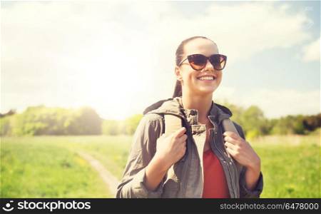 travel, hiking, backpacking, tourism and people concept - happy young woman in sunglasses with backpack walking along country road outdoors. happy young woman with backpack hiking outdoors. happy young woman with backpack hiking outdoors