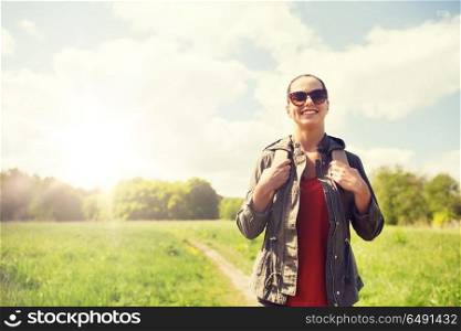 travel, hiking, backpacking, tourism and people concept - happy young woman in sunglasses with backpack walking along country road outdoors. happy young woman with backpack hiking outdoors. happy young woman with backpack hiking outdoors