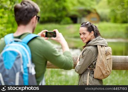 travel, hiking, backpacking, tourism and people concept - smiling couple with backpacks taking picture by smartphone in nature