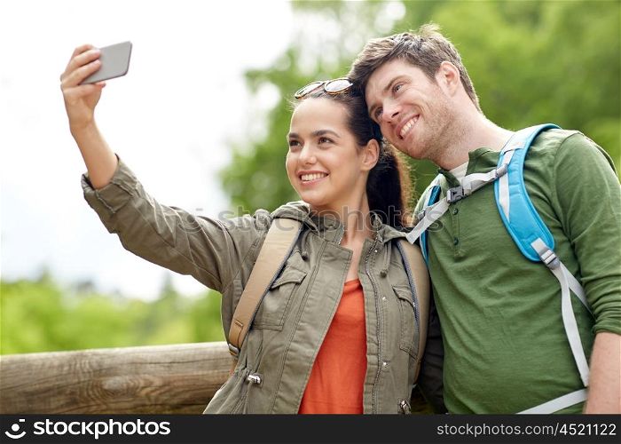 travel, hiking, backpacking, tourism and people concept - smiling couple with backpacks taking selfie by smartphone in nature