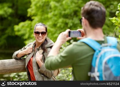 travel, hiking, backpacking, tourism and people concept - smiling couple with backpacks taking picture by smartphone in nature