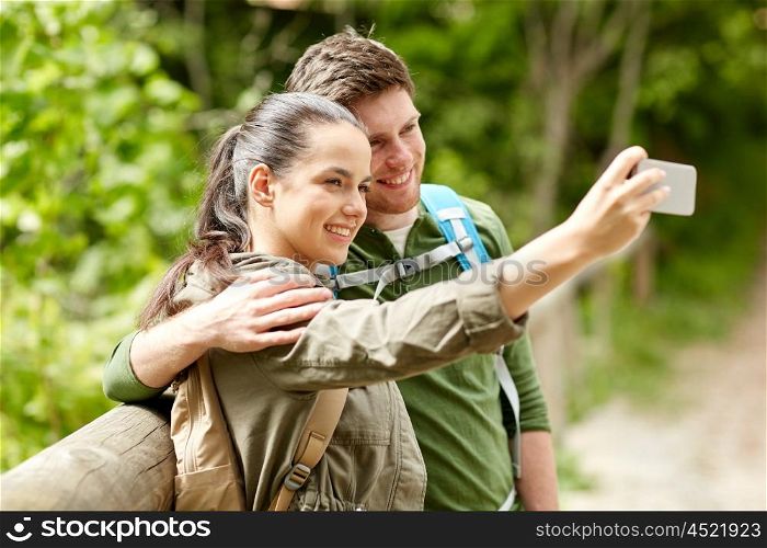 travel, hiking, backpacking, tourism and people concept - smiling couple with backpacks taking selfie by smartphone in nature