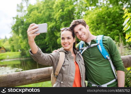 travel, hiking, backpacking, tourism and people concept - smiling couple with backpacks taking selfie by smartphone in nature