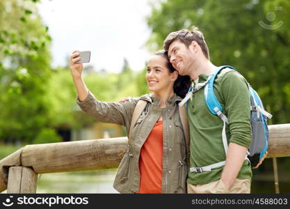 travel, hiking, backpacking, tourism and people concept - smiling couple with backpacks taking selfie by smartphone in nature