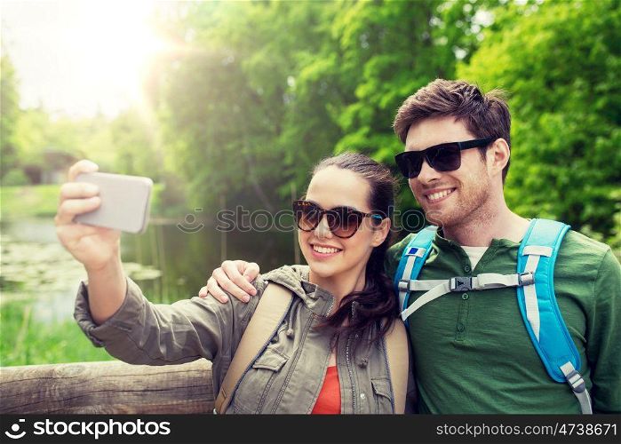 travel, hiking, backpacking, tourism and people concept - smiling couple with backpacks taking selfie by smartphone in nature. couple with backpacks taking selfie by smartphone. couple with backpacks taking selfie by smartphone