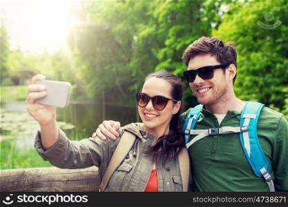 travel, hiking, backpacking, tourism and people concept - smiling couple with backpacks taking selfie by smartphone in nature. couple with backpacks taking selfie by smartphone. couple with backpacks taking selfie by smartphone