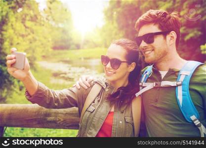 travel, hiking, backpacking, tourism and people concept - smiling couple with backpacks taking selfie by smartphone in nature. couple with backpacks taking selfie by smartphone