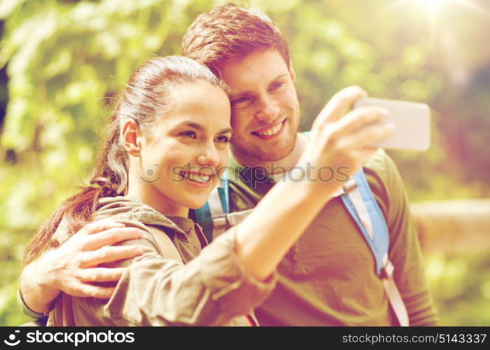 travel, hiking, backpacking, tourism and people concept - smiling couple with backpacks taking selfie by smartphone in nature. couple with backpacks taking selfie by smartphone