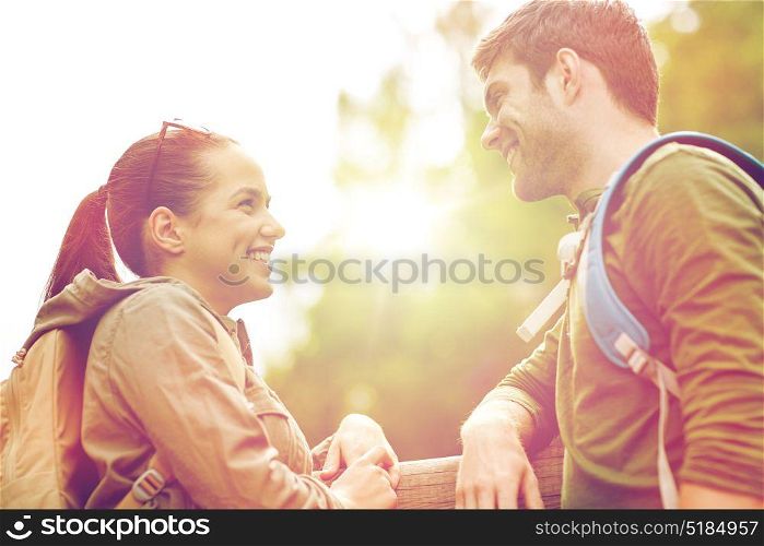 travel, hiking, backpacking, tourism and people concept - smiling couple with backpacks in nature looking and talking to each other. smiling couple with backpacks in nature