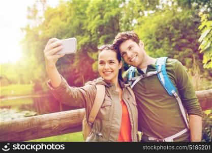 travel, hiking, backpacking, tourism and people concept - smiling couple with backpacks taking selfie by smartphone in nature. couple with backpacks taking selfie by smartphone