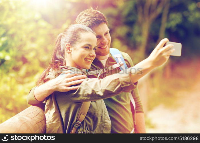 travel, hiking, backpacking, tourism and people concept - smiling couple with backpacks taking selfie by smartphone in nature. couple with backpacks taking selfie by smartphone