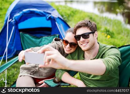 travel, hiking, technology, tourism and people concept - smiling couple of travelers taking selfie by smartphone at camping