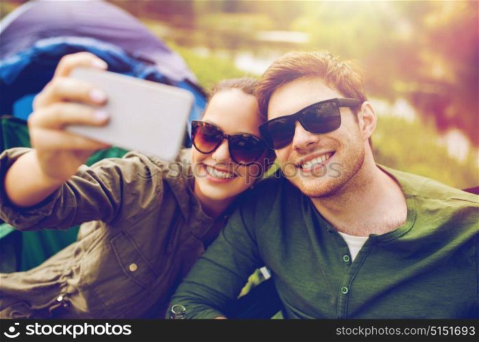 travel, hiking, technology, tourism and people concept - smiling couple of travelers taking selfie by smartphone at camping. couple of travelers taking selfie by smartphone