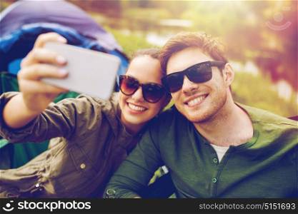 travel, hiking, technology, tourism and people concept - smiling couple of travelers taking selfie by smartphone at camping. couple of travelers taking selfie by smartphone