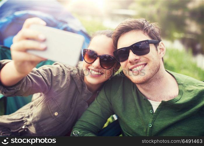 travel, hiking, technology, tourism and people concept - smiling couple of travelers taking selfie by smartphone at camping. couple of travelers taking selfie by smartphone. couple of travelers taking selfie by smartphone