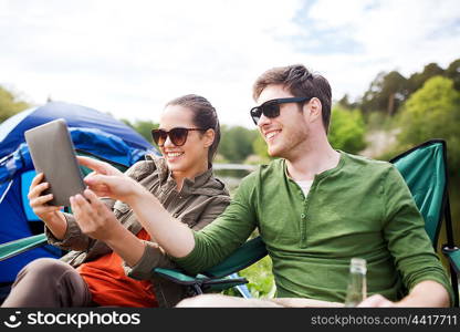 travel, hiking, technology, tourism and people concept - smiling couple with tablet pc computer sitting on chairs at camping tent