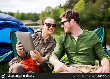 travel, hiking, technology, tourism and people concept - smiling couple with tablet pc computer sitting on chairs at camping tent