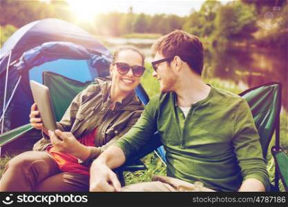 travel, hiking, technology, tourism and people concept - smiling couple with tablet pc computer sitting on chairs at camping tent