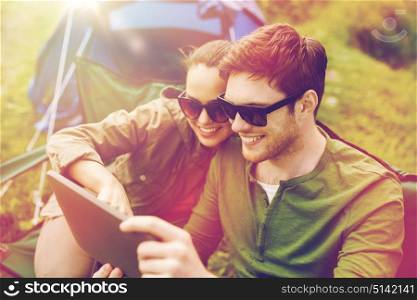 travel, hiking, technology, tourism and people concept - smiling couple with tablet pc computer sitting on chairs at camping tent. happy couple with tablet pc at camping tent