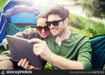 travel, hiking, technology, tourism and people concept - smiling couple with tablet pc computer sitting on chairs at camping tent. happy couple with tablet pc at camping tent. happy couple with tablet pc at camping tent