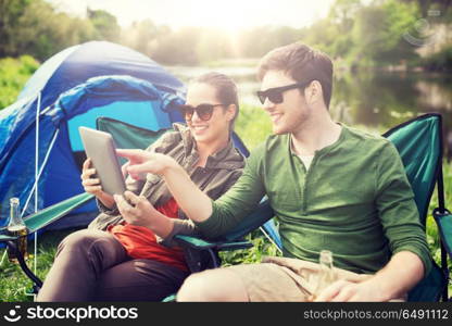 travel, hiking, technology, tourism and people concept - smiling couple with tablet pc computer sitting on chairs at camping tent. happy couple with tablet pc at camping tent. happy couple with tablet pc at camping tent