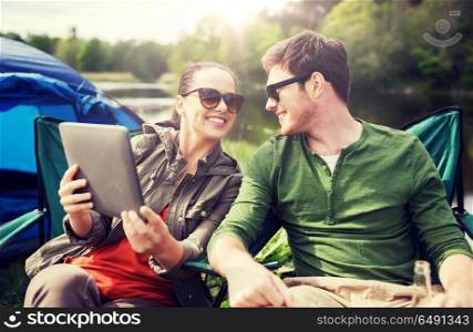 travel, hiking, technology, tourism and people concept - smiling couple with tablet pc computer sitting on chairs at camping tent. happy couple with tablet pc at camping tent. happy couple with tablet pc at camping tent