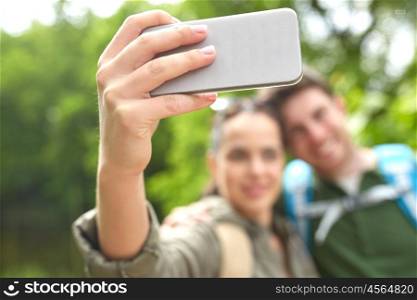 travel, hiking, tourism, technology and people concept - close up of happy couple with backpacks taking selfie by smartphone in nature