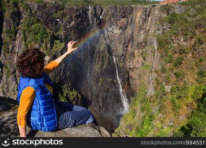 Travel, holidays. Tourist woman looking at Voringsfossen waterfall. and rainbow. Mabodalen canyon Norway. National tourist Hardangervidda route, Eidfjord sightseeing tour.. Tourist woman by Voringsfossen waterfall, Norway