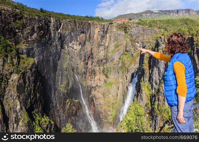 Travel, holidays. Tourist woman looking at Voringsfossen waterfall. Mabodalen canyon Norway. National tourist Hardangervidda route, Eidfjord sightseeing tour.. Tourist woman by Voringsfossen waterfall, Norway