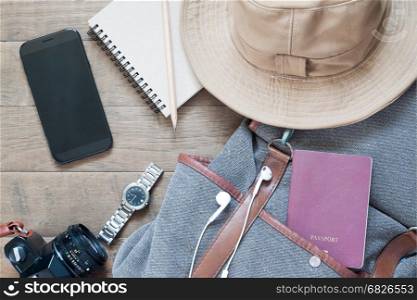 Travel items and accessories with mobile device on wood background, flat lay