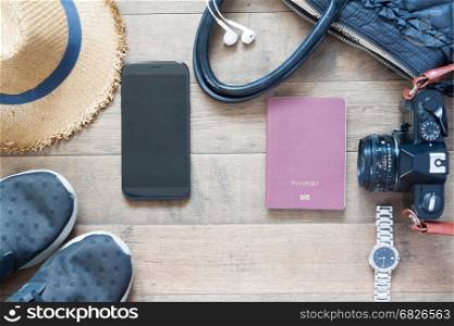 Travel items and accessories with mobile device on wood background, flat lay
