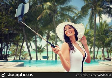 travel, leisure, summer, technology and people concept - sexy young woman taking selfie with smartphone over hotel resort swimming pool on beach background