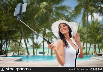 travel, leisure, summer, technology and people concept - sexy young woman taking selfie with smartphone over hotel resort swimming pool on beach background