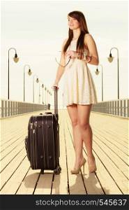 Travel, packing, journey concept. Woman wearing white short dress standing next to her suitcase thinking about adventure, pier in background.. Woman standing with suitcase, pier in background