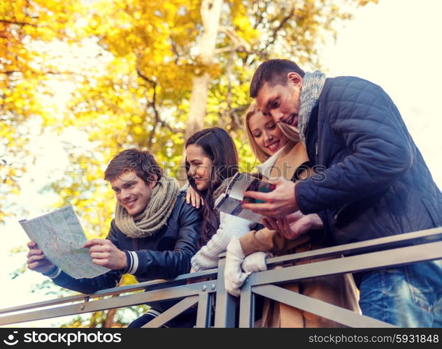 travel, people, tourism, and friendship concept - group of smiling friends with map and city guide standing on bridge in city park