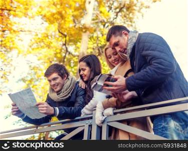 travel, people, tourism, and friendship concept - group of smiling friends with map and city guide standing on bridge in city park