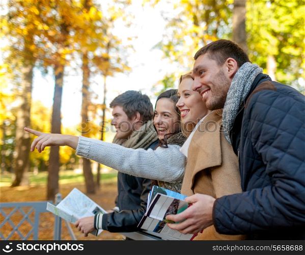 travel, people, tourism, gesture and friendship concept - group of smiling friends with map standing on bridge and pointing finger in city park