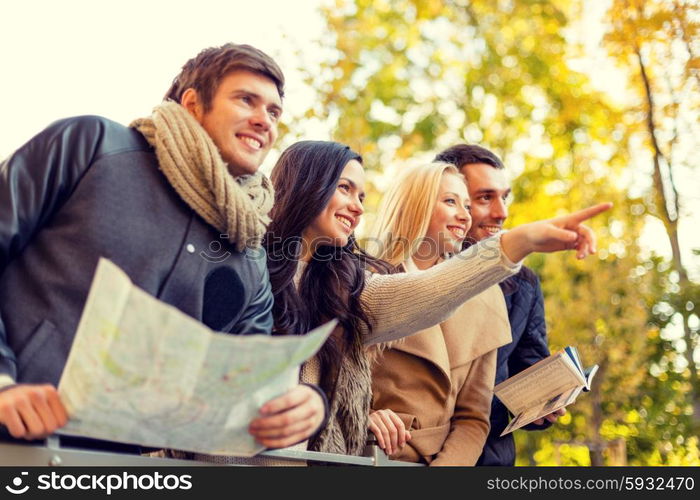 travel, people, tourism, gesture and friendship concept - group of smiling friends with map standing on bridge and pointing finger in city park