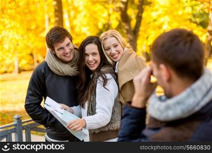 travel, people, tourism, photography and friendship concept - group of smiling friends with map taking picture in city park