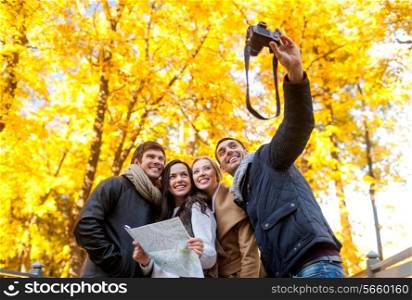 travel, people, tourism, technology and friendship concept - group of smiling friends with map and camera making self portrait in city park
