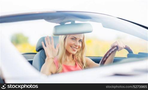 travel, road trip and people concept - happy young woman driving convertible car and waving hand. happy young woman driving convertible car